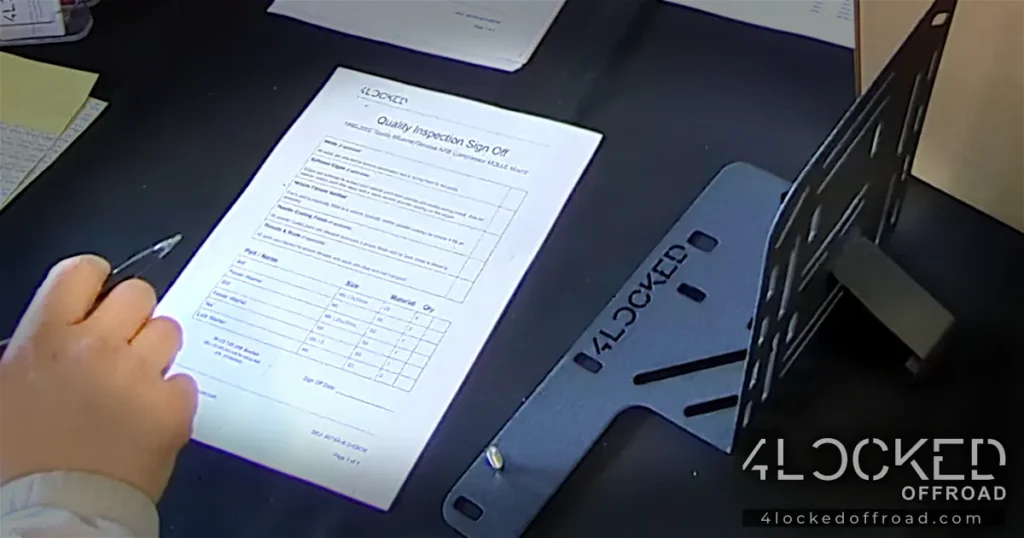 QA Sign-Off for ARB Bracket – 4Locked Offroad Hand signing a 4Locked Offroad QA sheet with an ARB bracket beside it during final inspection.